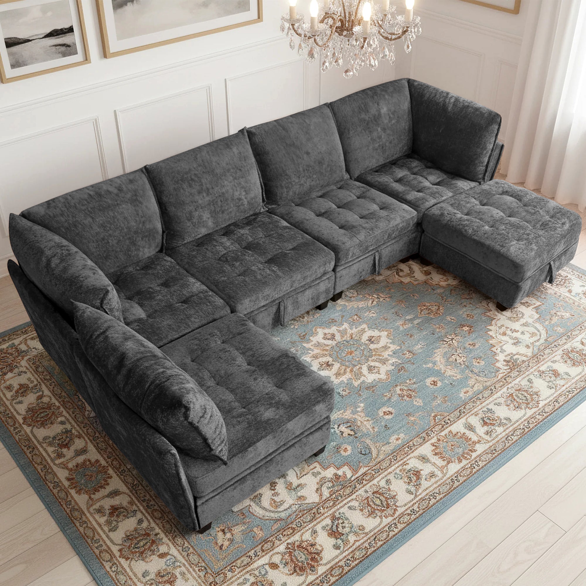Gray sectional sofa in a living room with a chandelier and framed pictures.