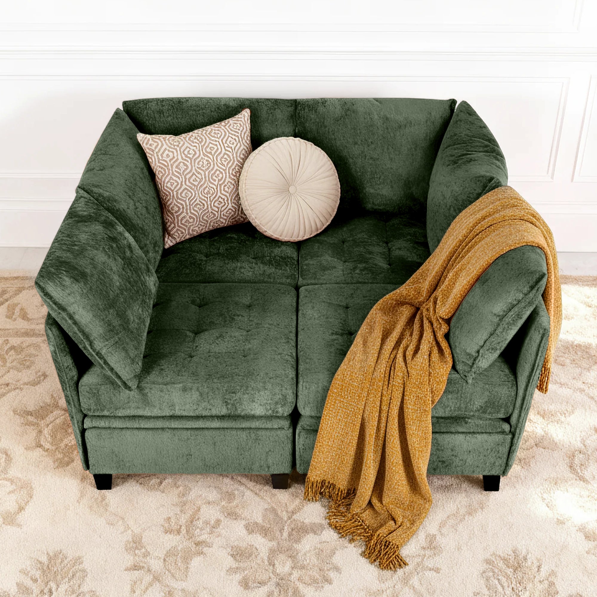 Green sofa with patterned cushions and a mustard yellow throw blanket on a beige carpet.