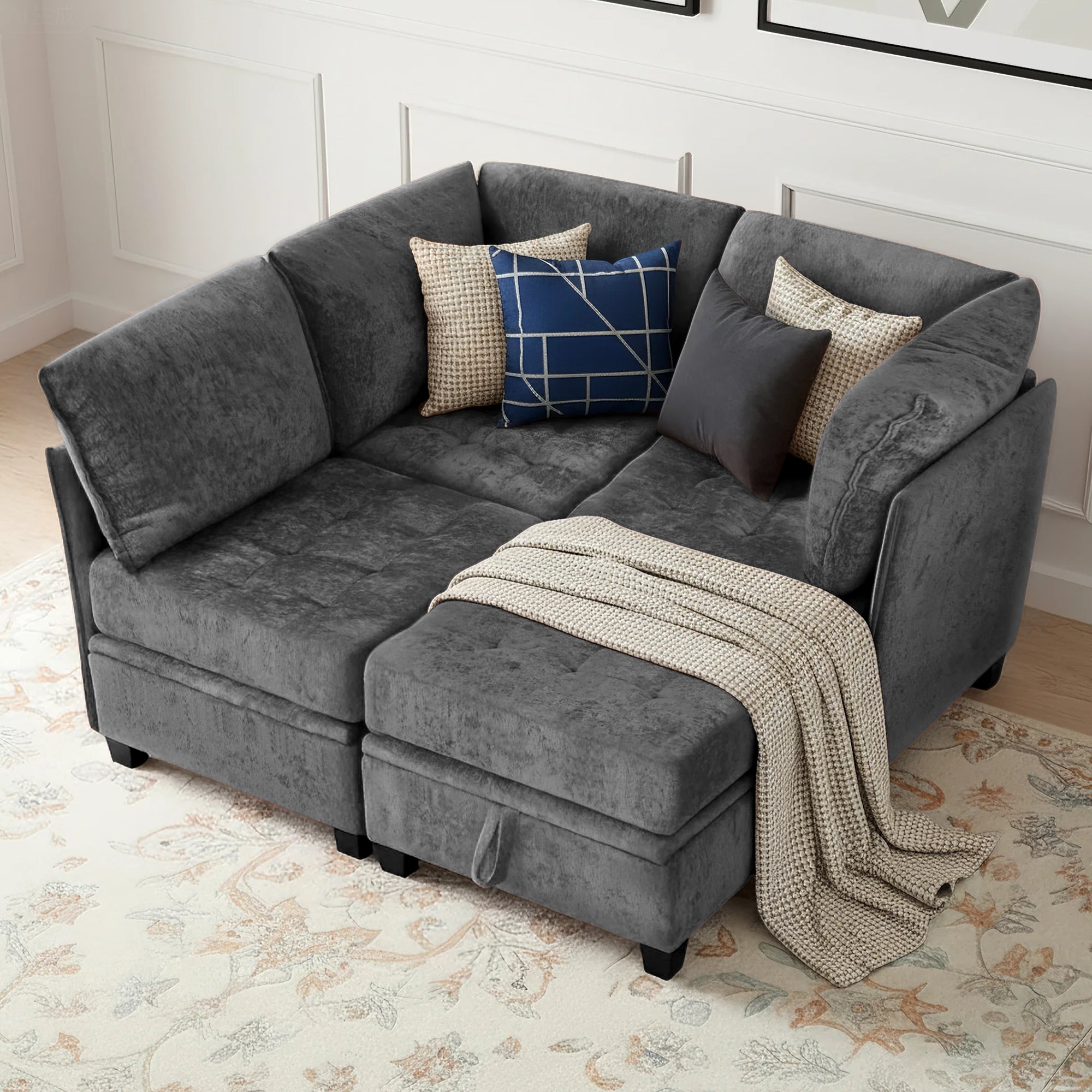 Gray sectional sofa with decorative pillows and a blanket on a patterned rug.