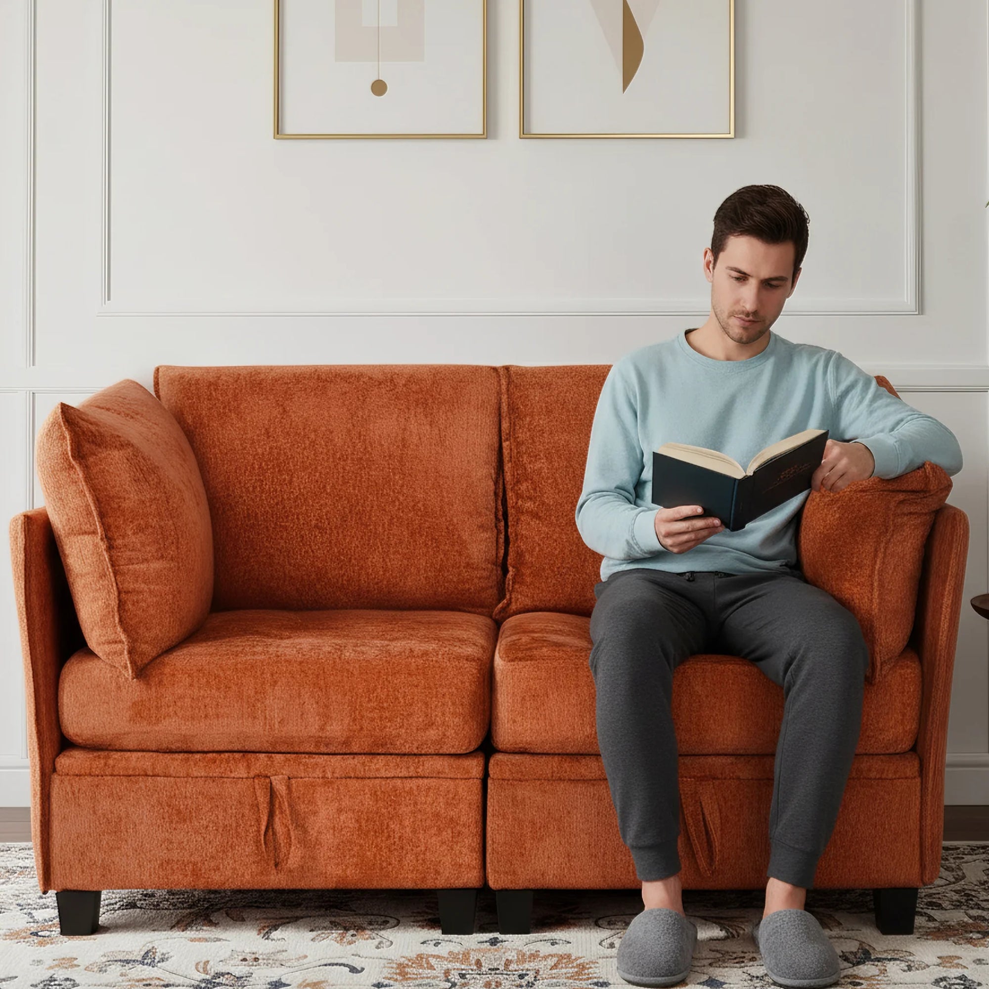 Man reading a book on an orange couch in a living room.