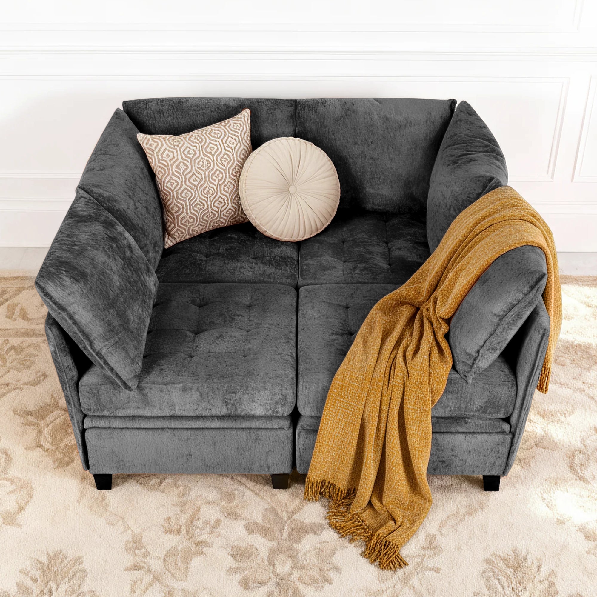 Gray sofa with decorative pillows and a mustard yellow throw blanket on a beige carpet.