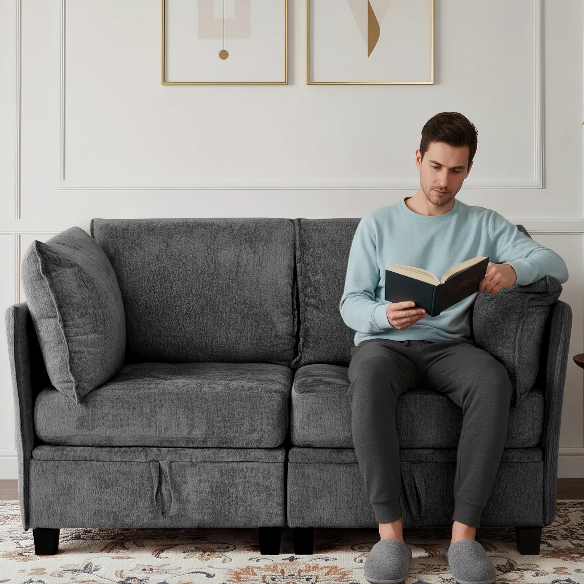 Man reading a book on a gray sofa in a living room.
