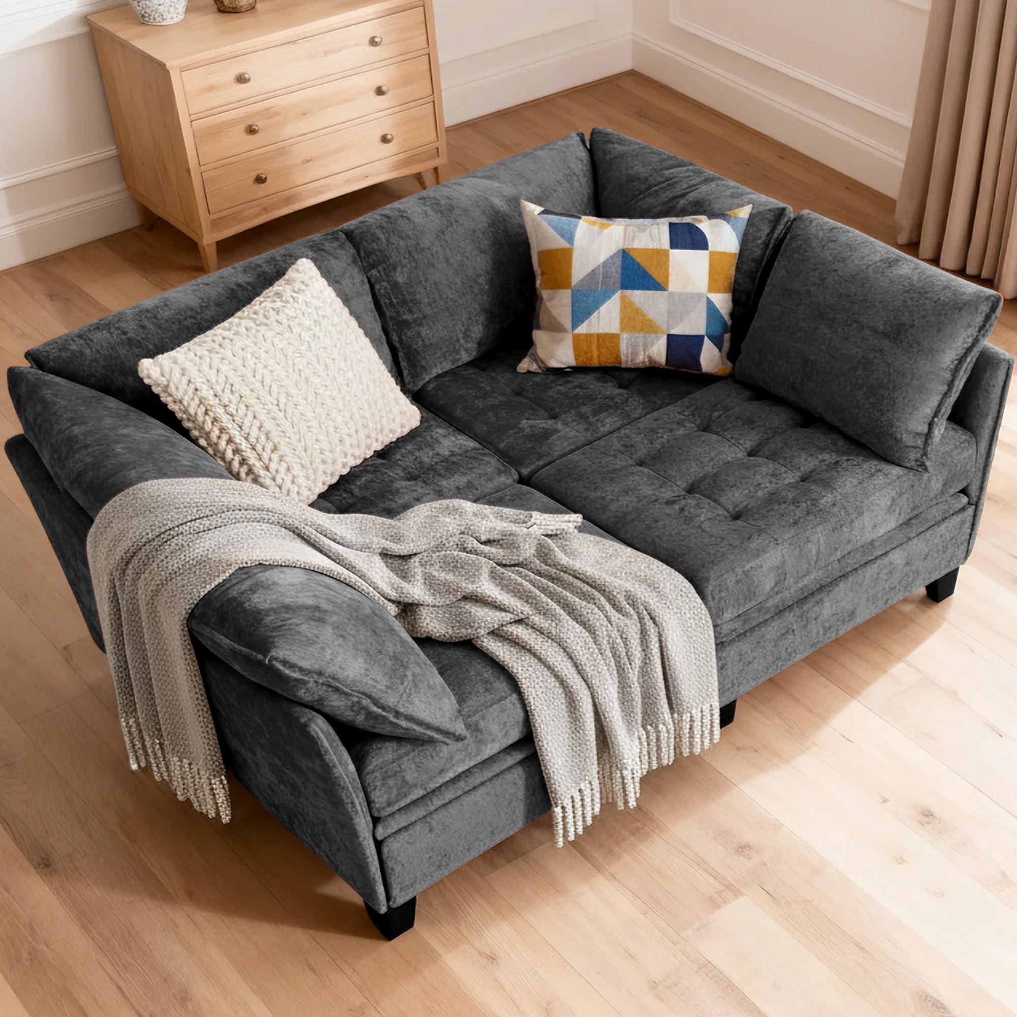 Gray sofa with cushions and a blanket on a wooden floor