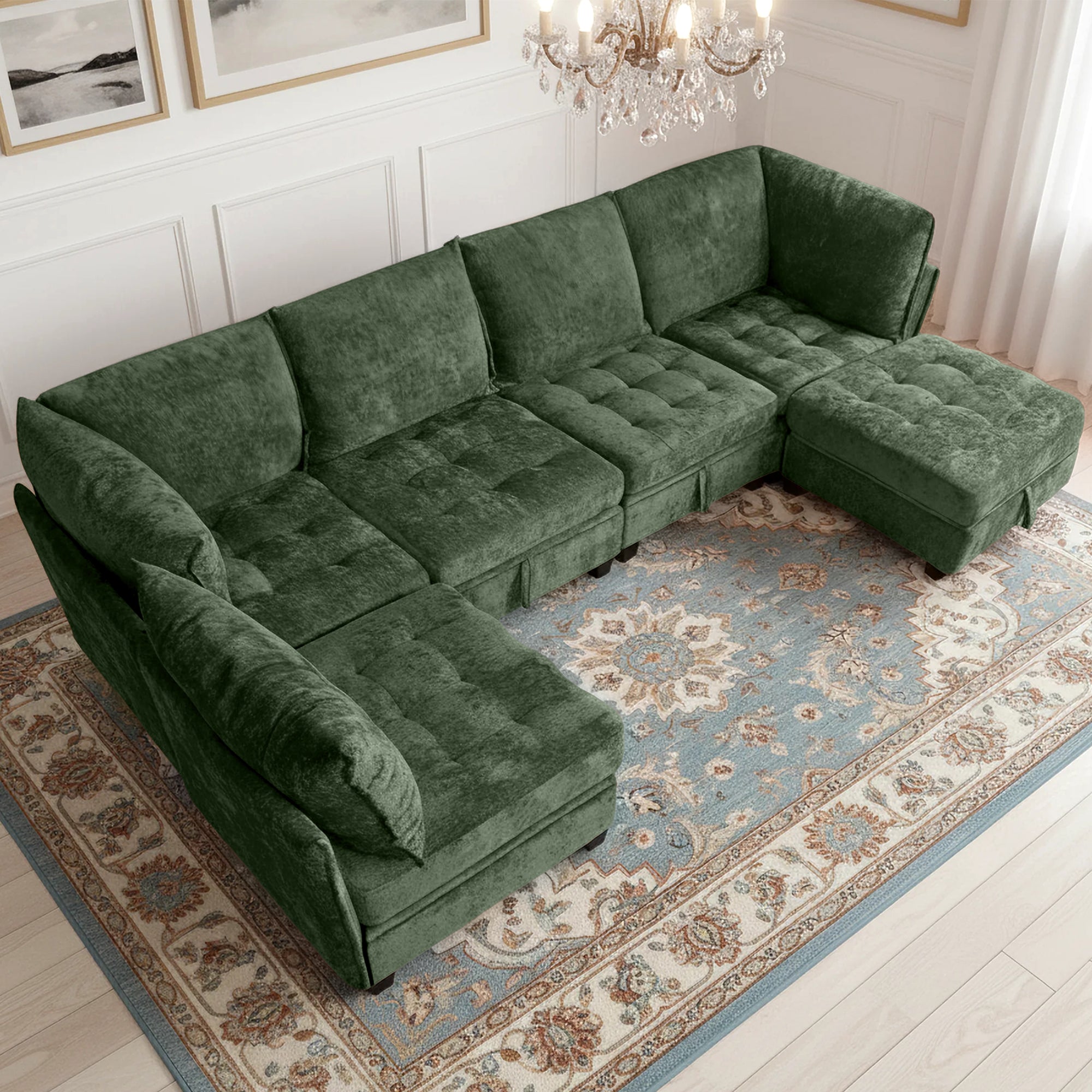 Green sectional sofa in a living room with a chandelier and framed pictures.