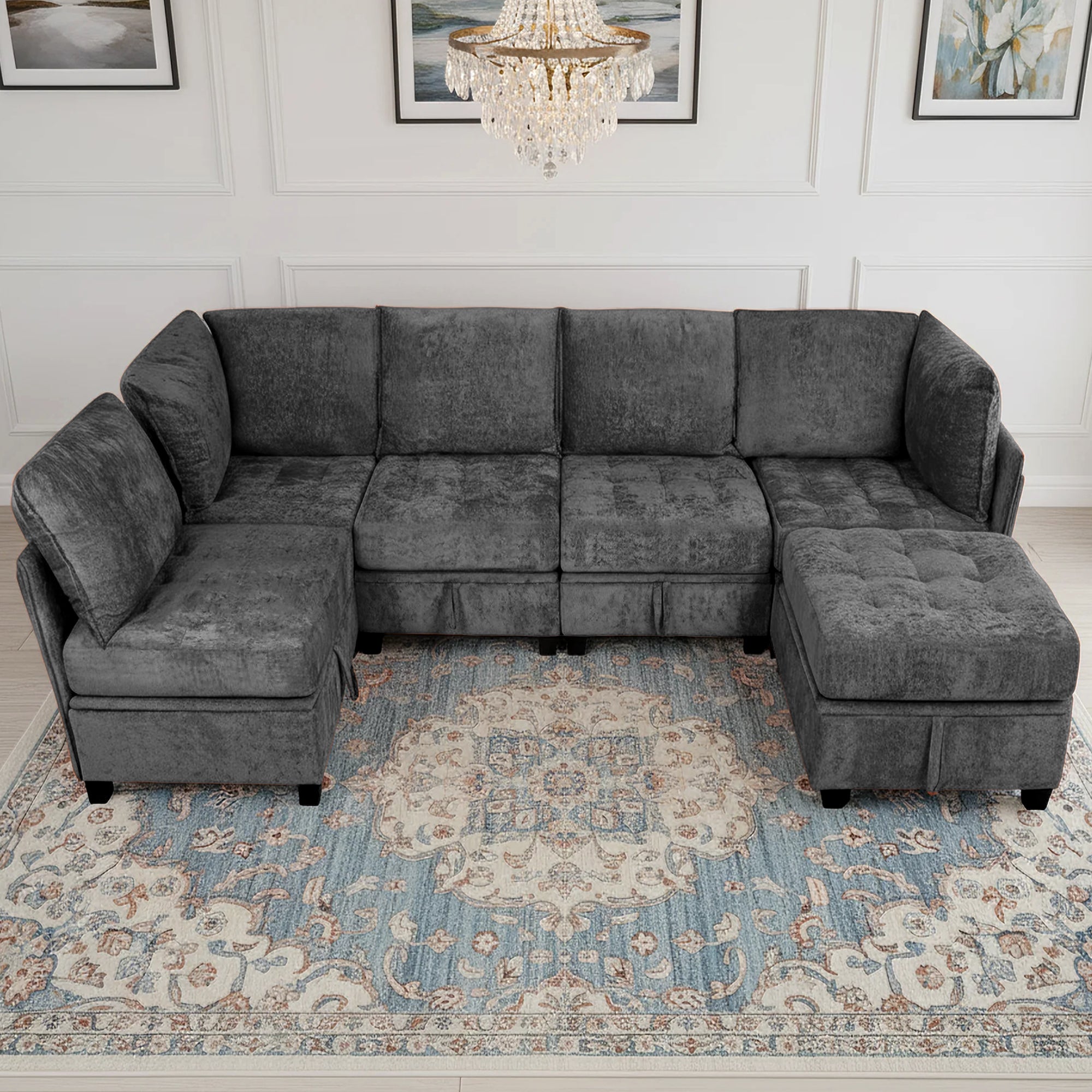 Gray sectional sofa in a living room with a chandelier and framed pictures on the wall.