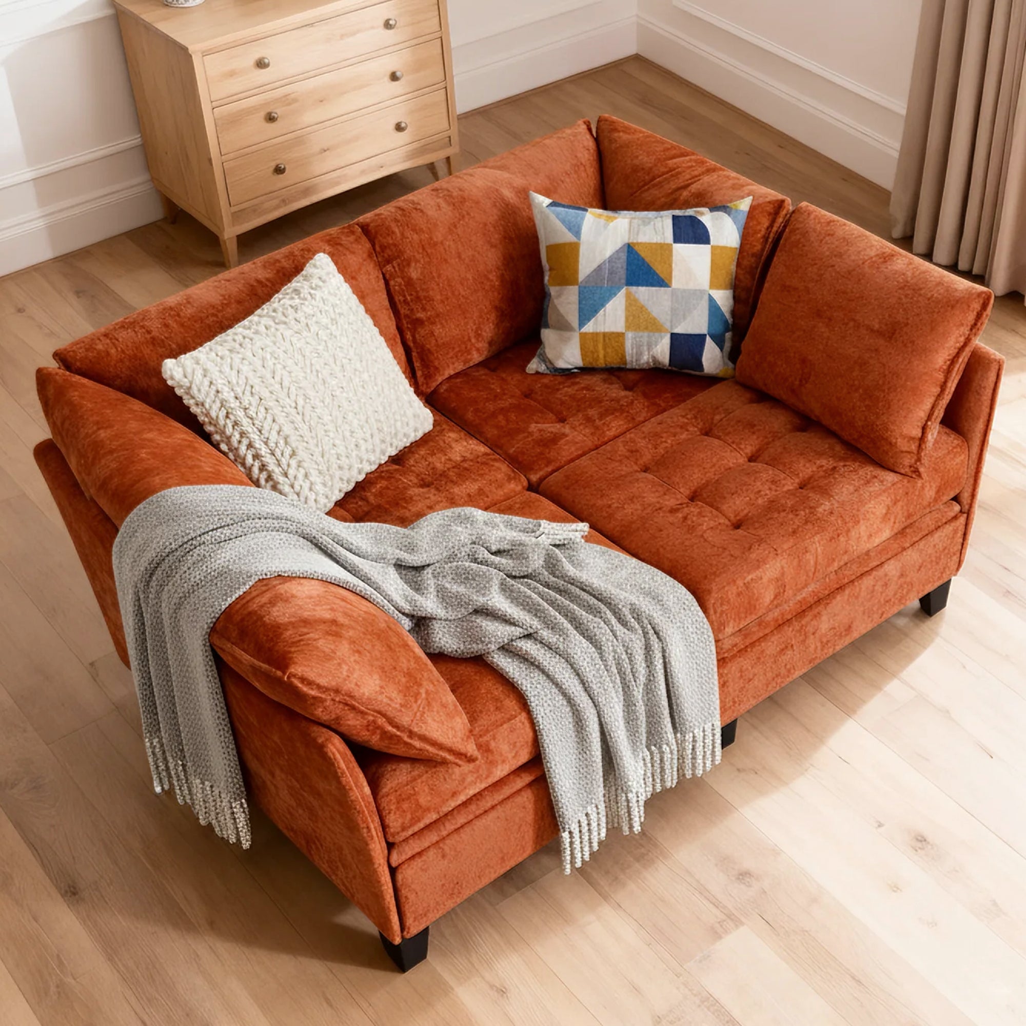 Orange sofa with cushions and a blanket on a wooden floor